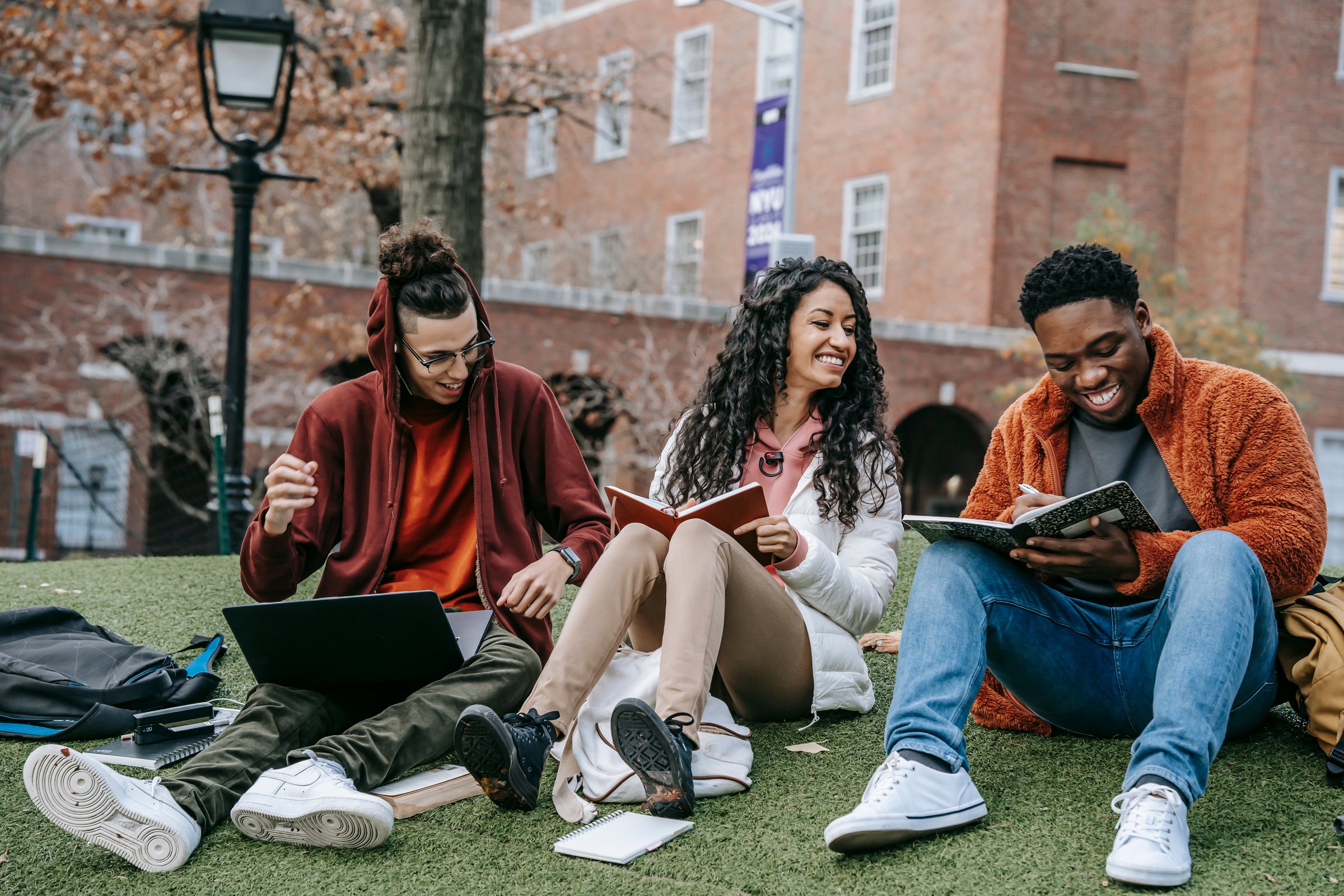 Cheerful multiethnic students with books sitting near university